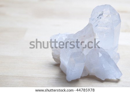 A clear quartz crystal cluster on a birch wood surface with copy space to the left.