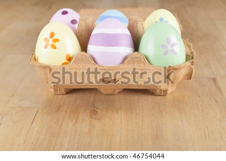 Six eggs, hand painted for Easter, placed in an open egg box.  Wooden table provides copy space.
