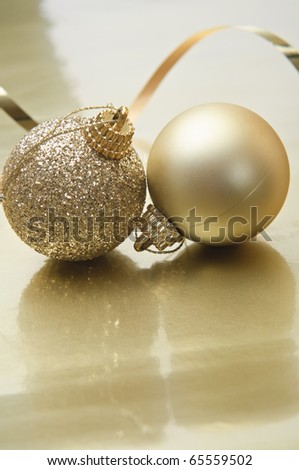 A pair of gold Christmas baubles, with swirling ribbon in background on a reflective metallic golden surface with copy space. Vertical orientation.