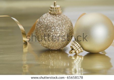 Two gold Christmas baubles to right of frame with spiraling foil ribbon in the background.  Set on a gold reflective metallic surface providing copy space below.