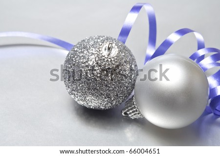 Two silver baubles on a metallic, reflective surface, with a swirled mauve ribbon in the background. Copy space.