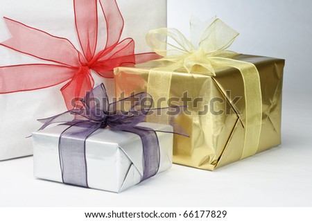 Close up of three gifts, wrapped in white and metallic foil papers, tied with ribbons and knotted with bows.