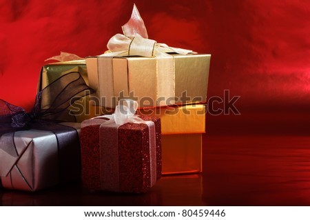 A selection of Christmas gifts, wrapped with tied ribbons against a metallic red background.  Copy space to right.  Horizontal (landscape) orientation.