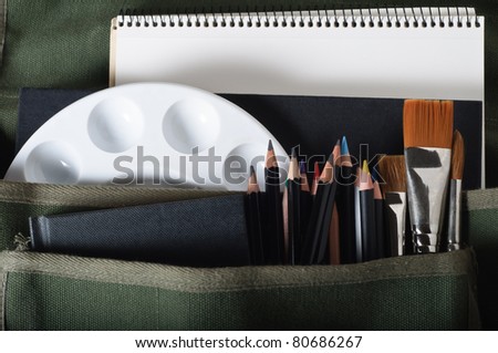 A pocketed canvas satchel bag filled with art materials.  Horizontal (landscape) orientation.
