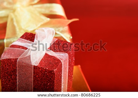 Close up of a glittery red gift box with white ribbon.  Gold box and bow in the background.  Red copy space to right.
