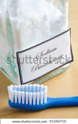A bottle of sodium bicarbonate (baking soda) and a toothbrush on a wooden surface, to illustrate non-toxic dental care or natural toiletries.