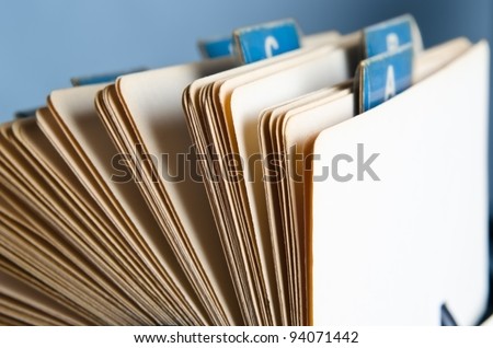 Close up angled side view of an old, yellowing rotary card index with worn blue alphabetical tabs against a light blue background.  Copy space angles away from viewer on right-hand side.