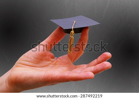 Person\'s hand holding a miniature graduation cap\ -- Education or career concept