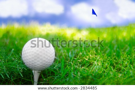 Golf ball on a tee with flag in the distance, against blue sky