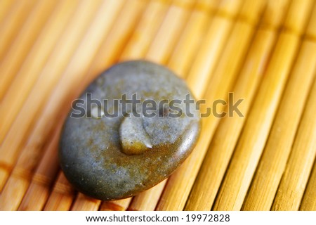 river stone with water drop, closeup, on bamboo