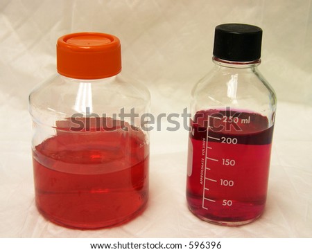 Two lab bottles, one glass and one plastic, filled with red media, in a laboratory environment.