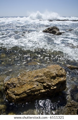 Vertical image of a rocky beach with a wave crashing in the background.