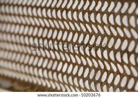 Close up of a metal grid with holes in a honeycomb pattern.  Part of a rusted fence