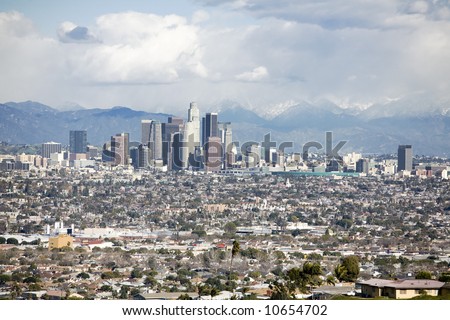 Downtown Los Angeles skyline with smaller buildings and homes in the forground and mountains in the background.