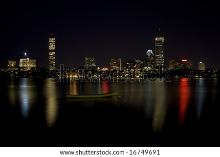 Night image of the Boston Skyline with a small boat in the foreground on the Charles River