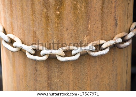 A rusty chain fastened on a rusty pillar at a harbor.