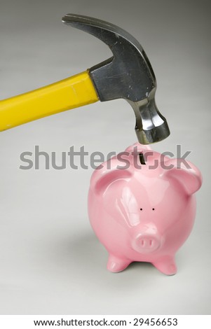 Vertical image of a piggy bank about to be smashed open with a hammer.