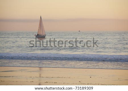 Horizontal image of a sailboat on the ocean near the beach during dusk.