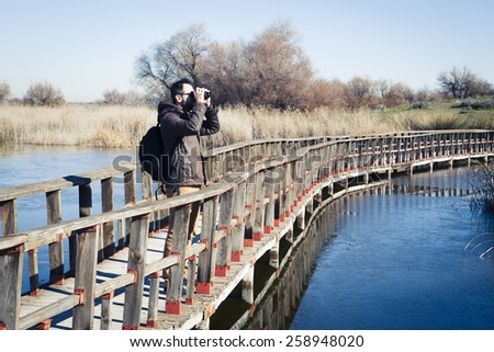 Man watching nature with binoculars, in a wood bridge over the water.