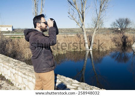 Man watching nature with binoculars next to the river.