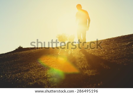 Man with his dog. Dog is sitting on the grass, looking to the man eyes. Back lit.