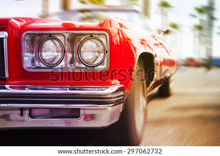 Red classic sports car driving fast, with motion blur background. Close up view.
