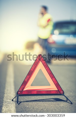 Emergency triangle in the middle of the road. Man and car in the background.