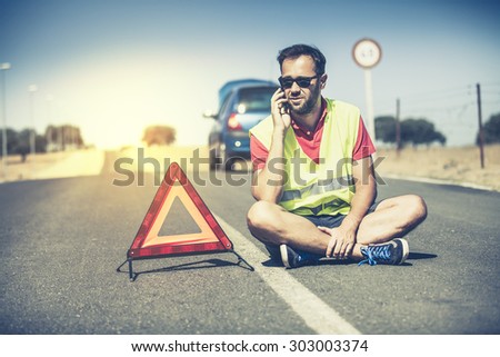 Sitting man talking by phone in the middle of the road after car breakdown.