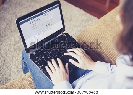 MALAGA, SPAIN - APRIL 26, 2015: Facebook login page in a computer screen. Woman holding a laptop on her knees while type on the keyboard. Facebook is the most famous social website all over the world.