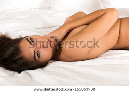 Beautiful petite Eurasian woman lying nude in bed