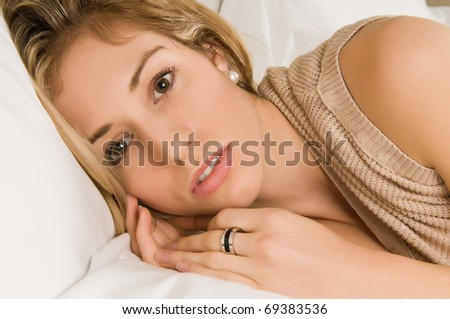 Beautiful young blonde in bed in a tan knit blouse
