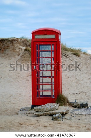 An old red British pay telephone box on a sandy beach.