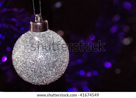 A silver glittery Christmas tree bauble, with purple and blue tinsel in the background.