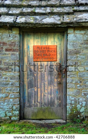 An old door with a notice asking people not to pick the wild flowers