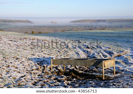 Corfe Castle, Dorset, in the background, surrounded by mist. in the foregrouns, a farmer\'s field covered in a dusting of snow.