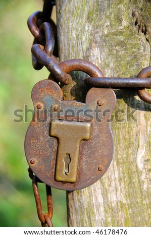 A detailed image of a large, strong old padlock, locking a chain around a wooden post
