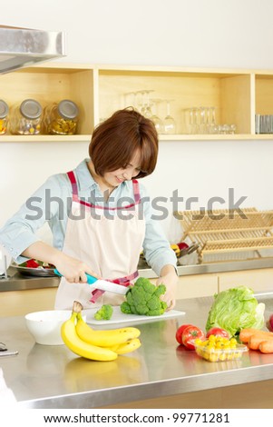 Beautiful young woman in kitchen making salad. Portrait of asian woman.