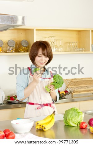 Beautiful young woman in kitchen making salad. Portrait of asian woman.