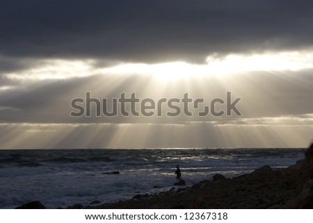 Fishing at the break of day at Montauk Point, Long Island. Sunrays finding a opening though the clouds.