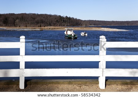 Two small boats framed by a white wooden fence, The harbor is starting to freeze over. Cold Spring Harbor, Long Island , New York