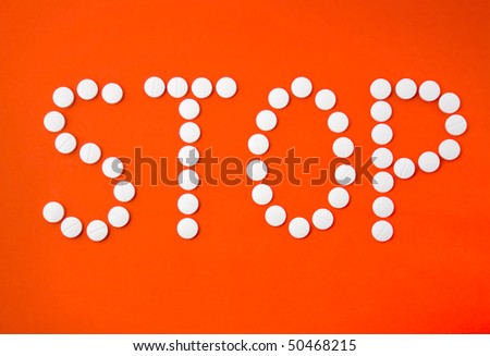 Word STOP written with white pills on red paper background