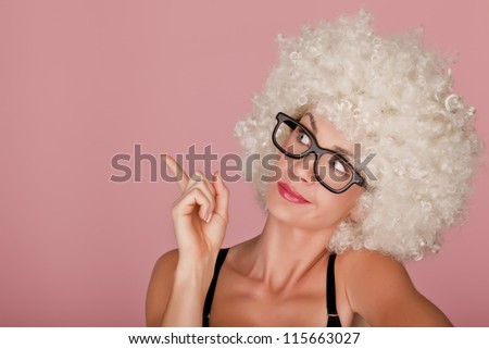 Playful and funny woman wearing a curly wig on a pink background. Funny face.
