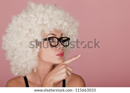 Playful and funny woman wearing a curly wig on a pink background. Funny face.