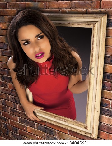 A concept of a beautiful woman trapped in a picture frame hanging on a brick wall looking out. What is out there.