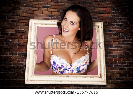A concept of a beautiful woman trapped in a picture frame hanging on a brick wall looking out.
