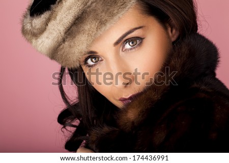Beauty in fur. A beautiful woman wearing a warm fur coat on a pink background.