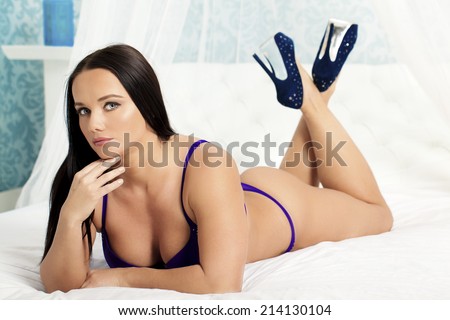 A sexy woman wearing lingerie and high heels relaxing on a bed.