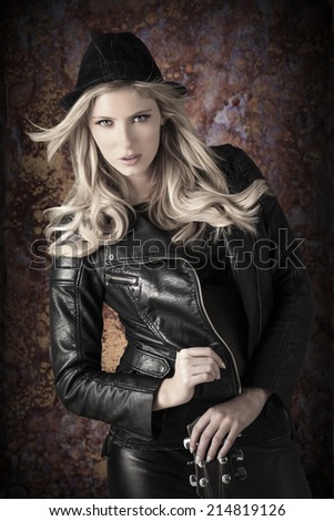 Beautiful blond woman wearing black leather and holding a guitar over a grunge rusted background.