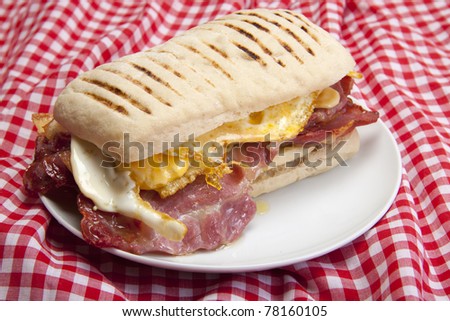 Home made panini with egg and bacon on a small white plate, ready to be eaten.