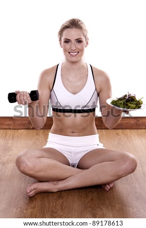 Healthy living. A Young blond fitness woman doing exercise and holding a plate of fresh salad.